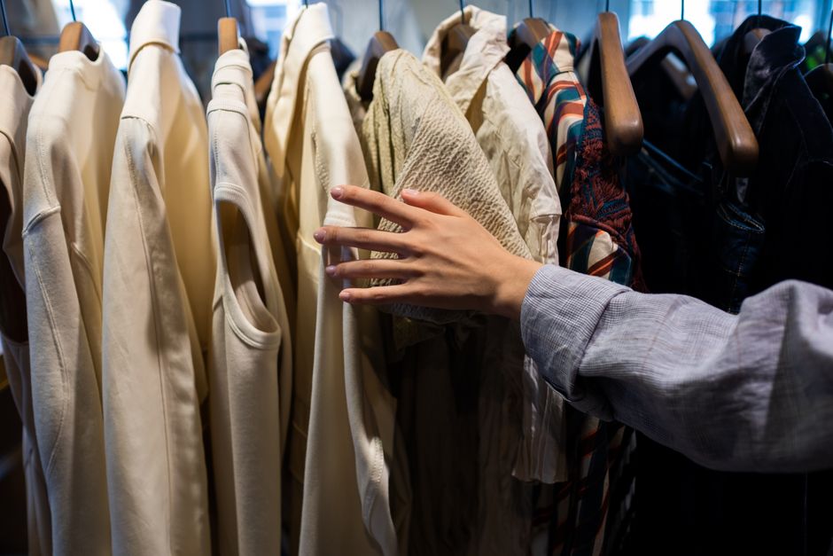 A shopper's hand browsing clothes in a retail store, focusing on fabric textures.