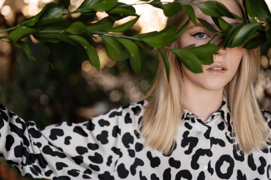 A blonde woman in a leopard print shirt partially obscured by green leaves