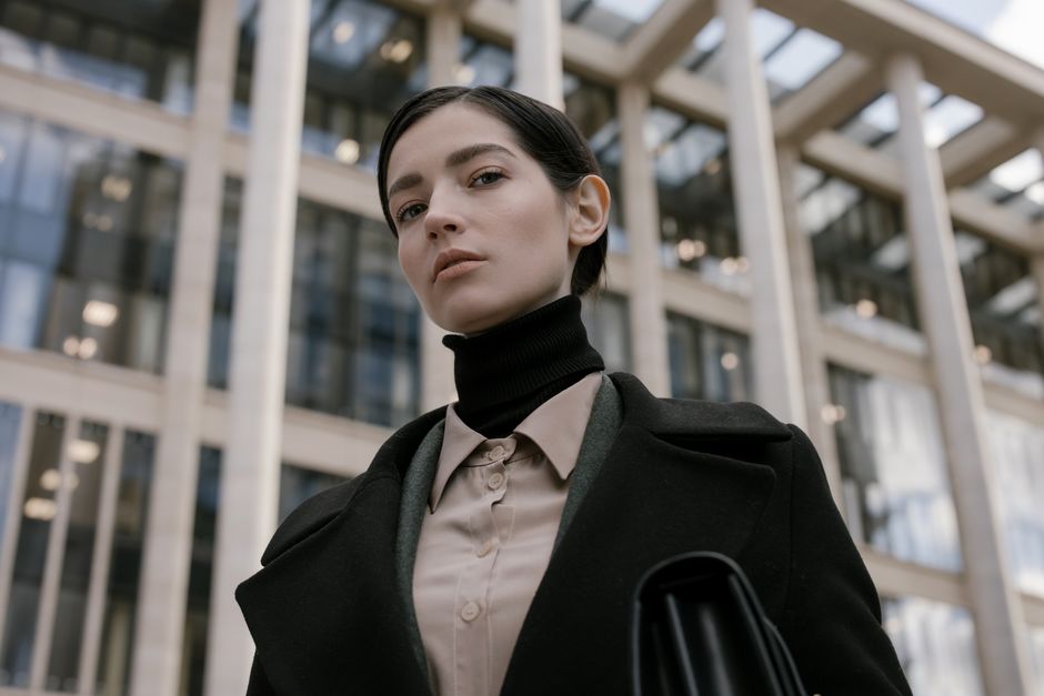 A fashionable young woman in professional attire with urban architecture background