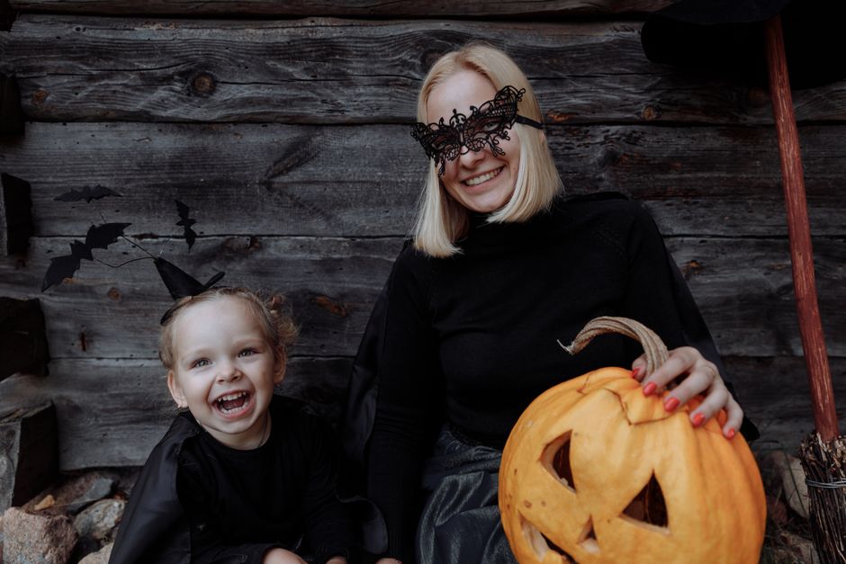A joyful mother and daughter in Halloween costumes with a carved pumpkin and wooden background