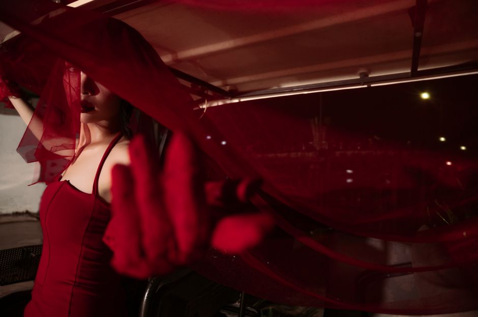 A mysterious woman in a red dress and veil with dramatic lighting