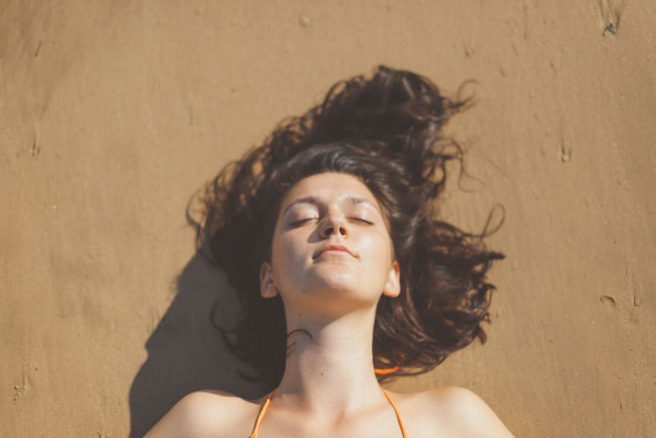 A serene portrait of a woman with closed eyes enjoying the sun on a sandy beach in Weligama, Sri Lanka