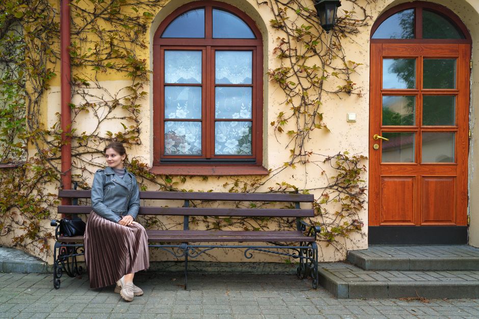 A stylish woman sits on a bench near an ivy-covered wall in Pinsk, Belarus. Elegant and tranquil setting