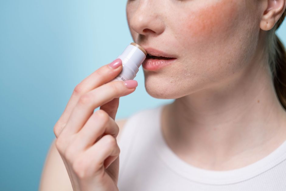 A woman applying lip balm to her lips, highlighting skincare and self-care routine