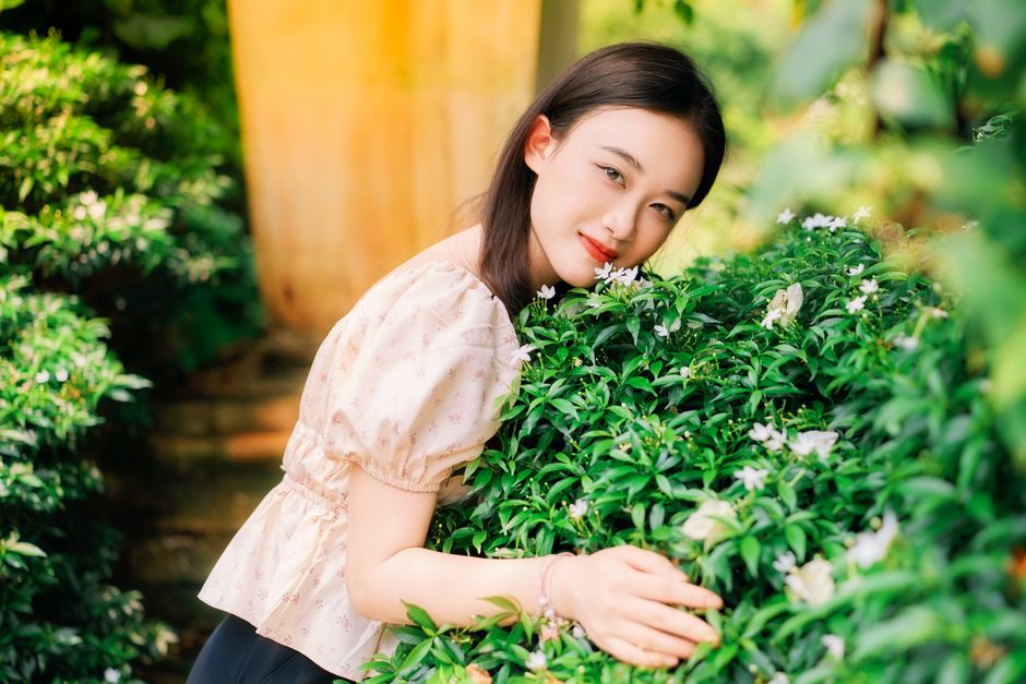 A woman enjoying a serene moment in a lush garden filled with greenery and flowers