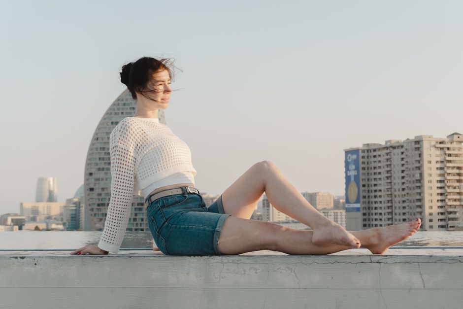 A woman enjoys a sunny day on a rooftop, showcasing casual fashion against a cityscape backdrop