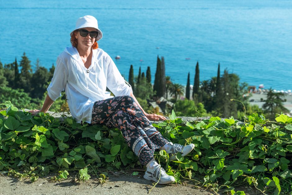 A woman enjoys a tranquil summer day by the sea, surrounded by lush greenery and a beautiful landscape