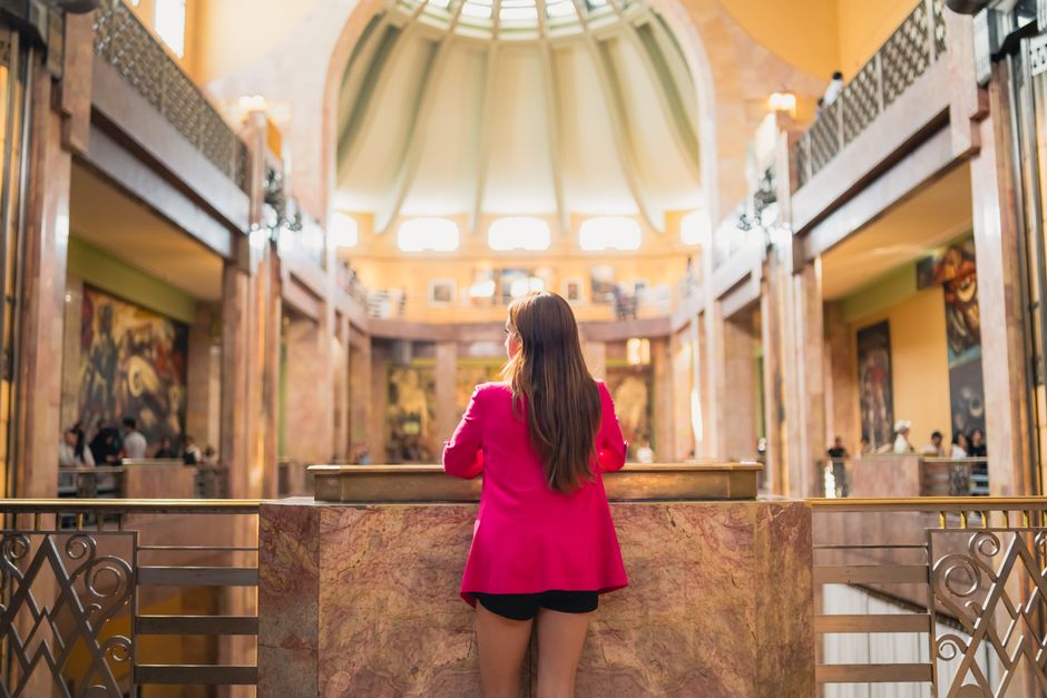 A woman in a pink jacket explores an Art Deco interior in Mexico City