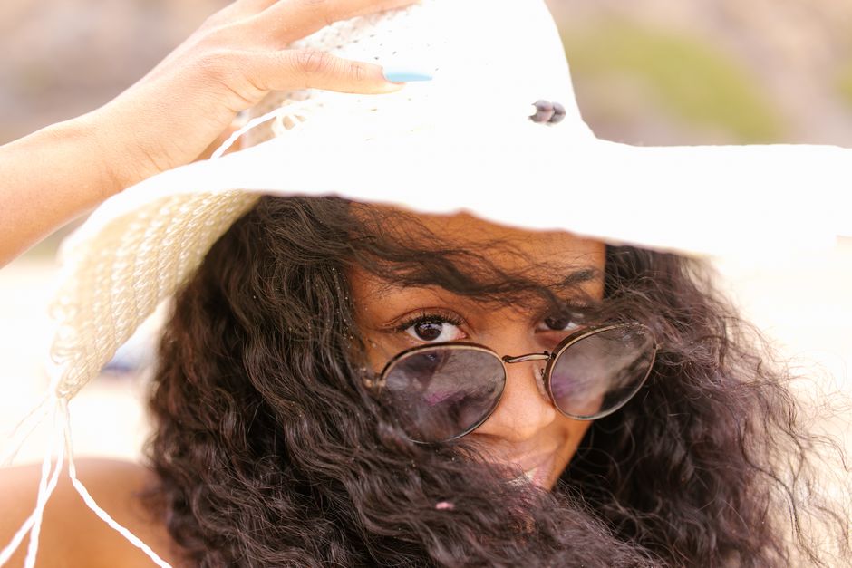 A woman playfully adjusts her straw hat while wearing sunglasses on a sunny day. Perfect for summer lifestyle
