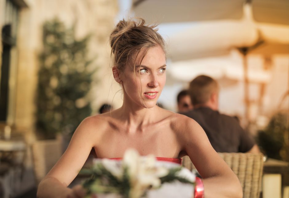 A woman sits in an outdoor cafe, enjoying a sunny day. She appears relaxed and thoughtful, embodying a sense o