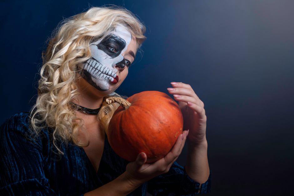 A woman with skull face paint holding a pumpkin, capturing the eerie essence of Halloween