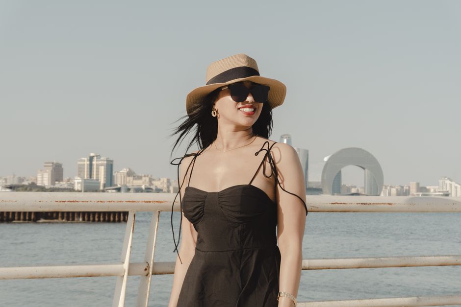 Woman in summer outfit enjoying a sunny day by the Baku waterfront with city skyline in the background.