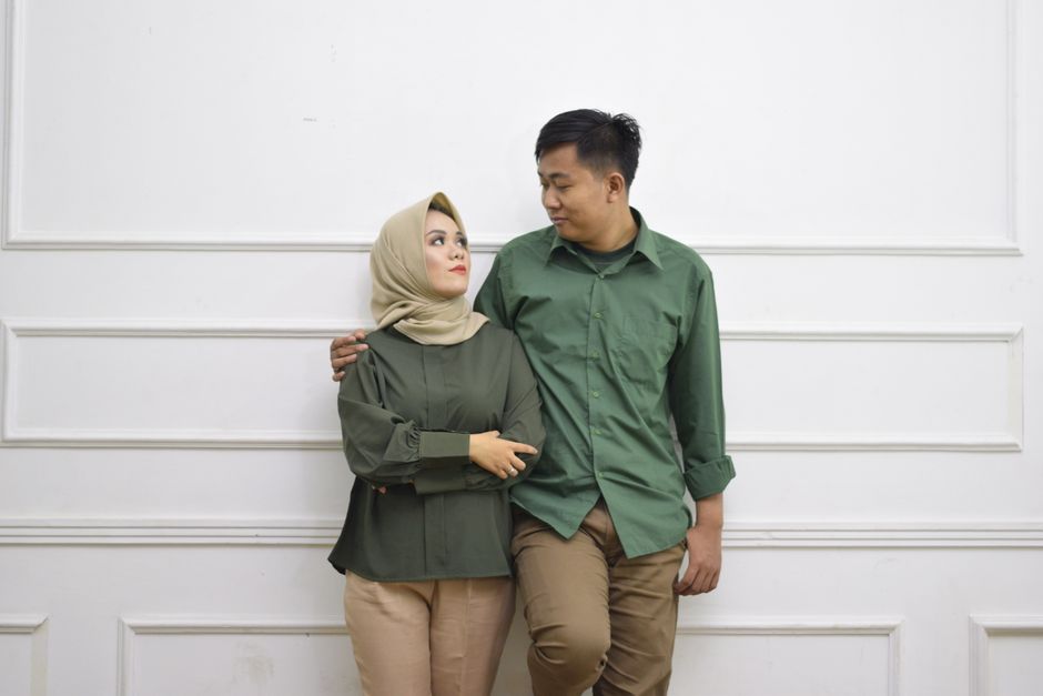 An affectionate couple poses against a white wall, showcasing a modern fashion style
