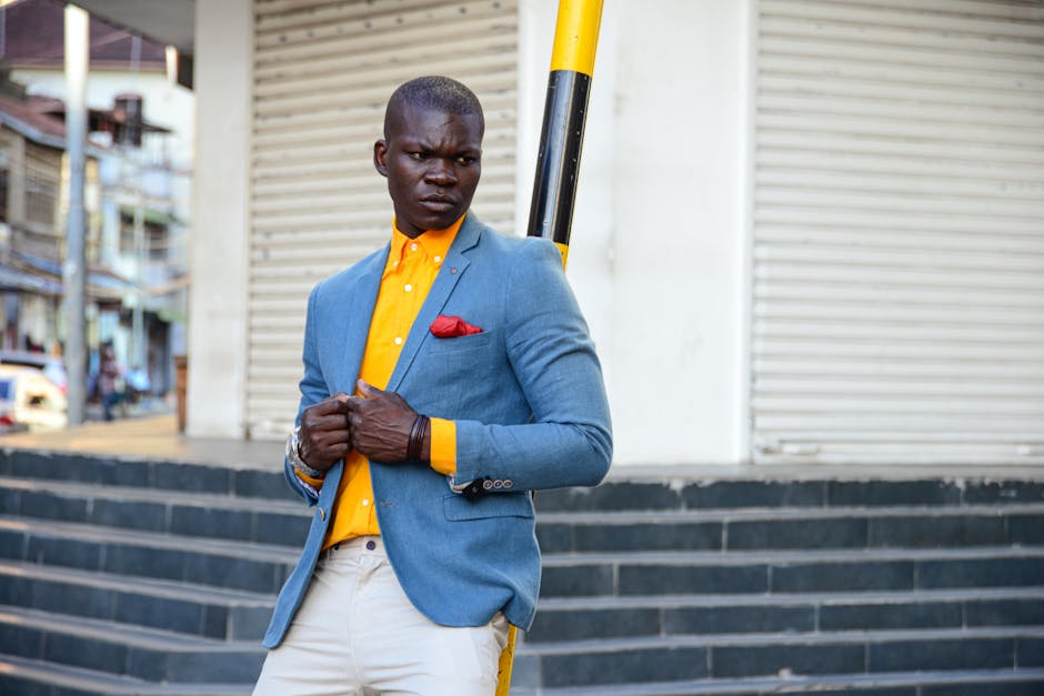 Confident man in blue blazer and orange shirt posing against urban backdrop with stairs and roller shutters.