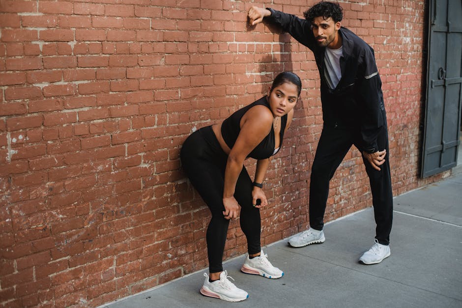 Man and woman in sportswear posing confidently against a classic brick wall.