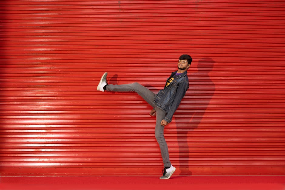 Man in denim jacket striking a pose against a vibrant red corrugated wall in urban setting.