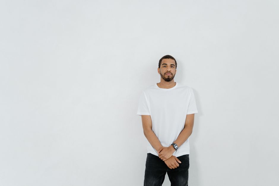 Portrait of a casual young man in a white shirt standing against a plain background, ample copy space available.