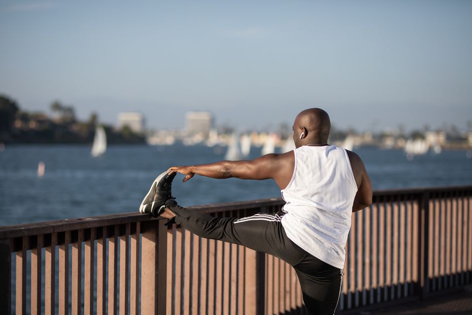 African American man stretching by the water, promoting outdoor fitness and healthy lifestyle.