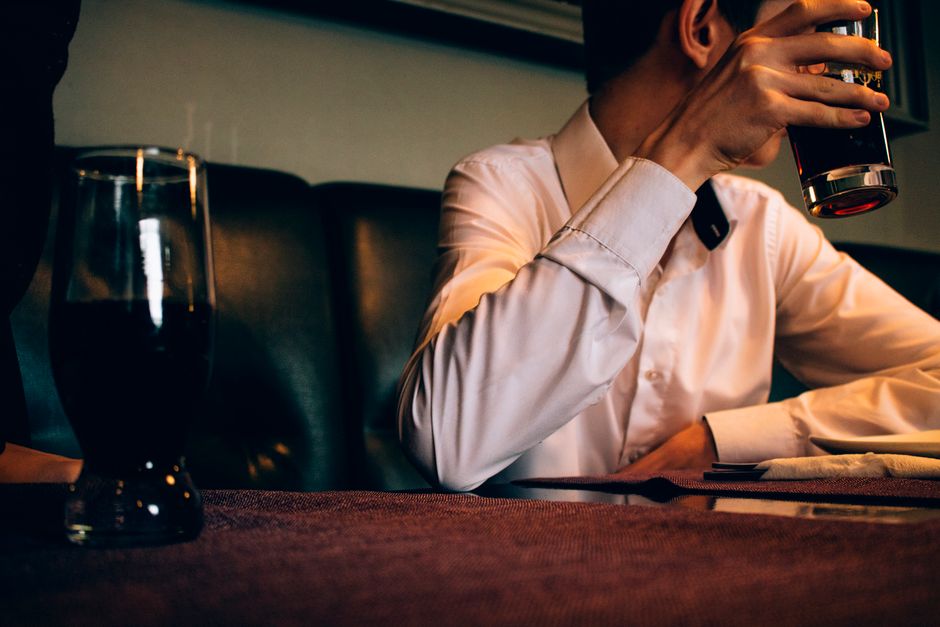 Adult man in white shirt holding a drink indoors. Warm, relaxed ambiance.