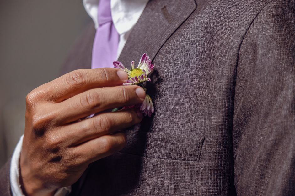 Close-up of a groom adjusting his flower boutonniere, symbolizing wedding elegance.