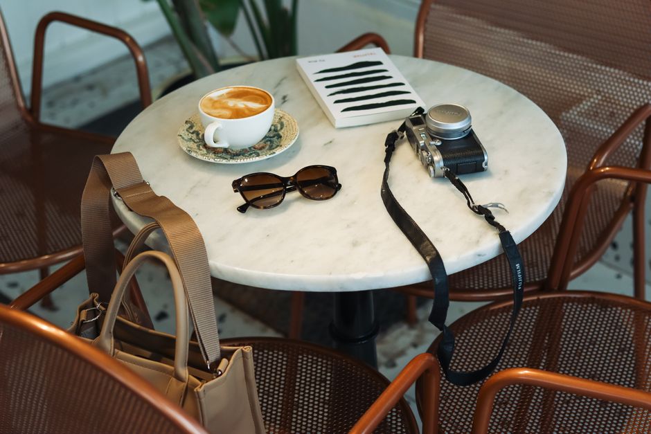 A stylish cafe setup with cappuccino, camera, and sunglasses on a marble table.