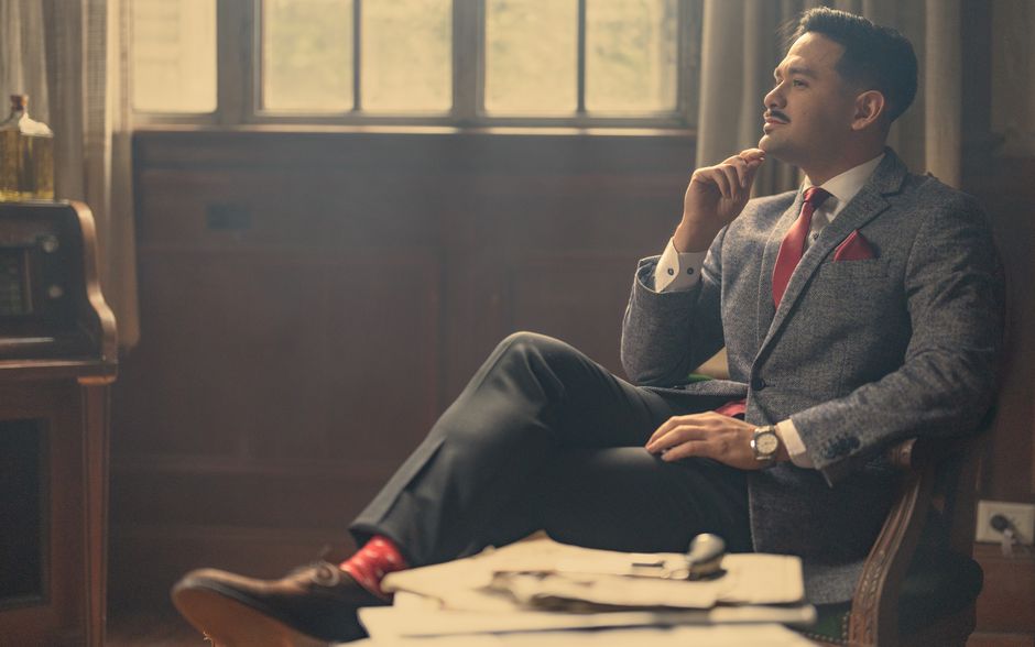 A stylish man in a suit sits thoughtfully in a vintage office, exuding confidence and elegance.
