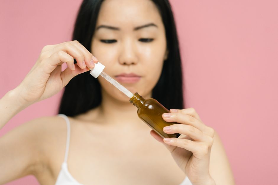 Close-up of a woman holding a serum bottle with a dropper, focusing on skincare