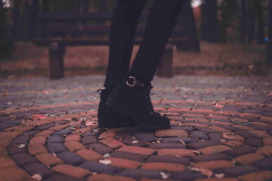 A stylish pair of black boots on a patterned stone walkway during fall.
