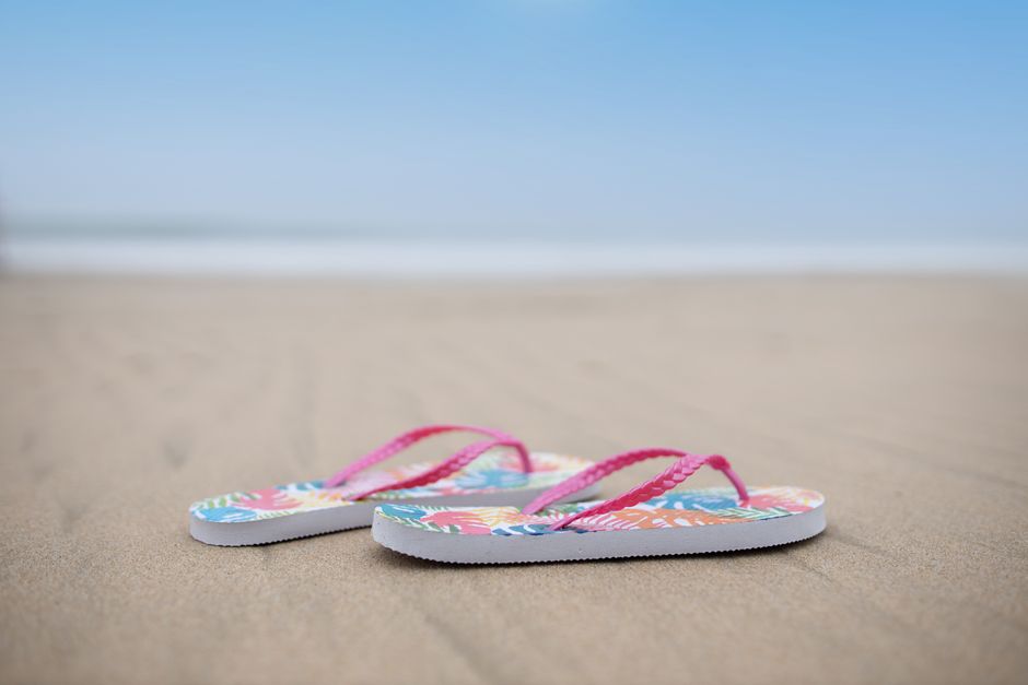 Colorful flip flops resting on a sandy beach with a blue sky overhead, capturing a perfect summer vibe.