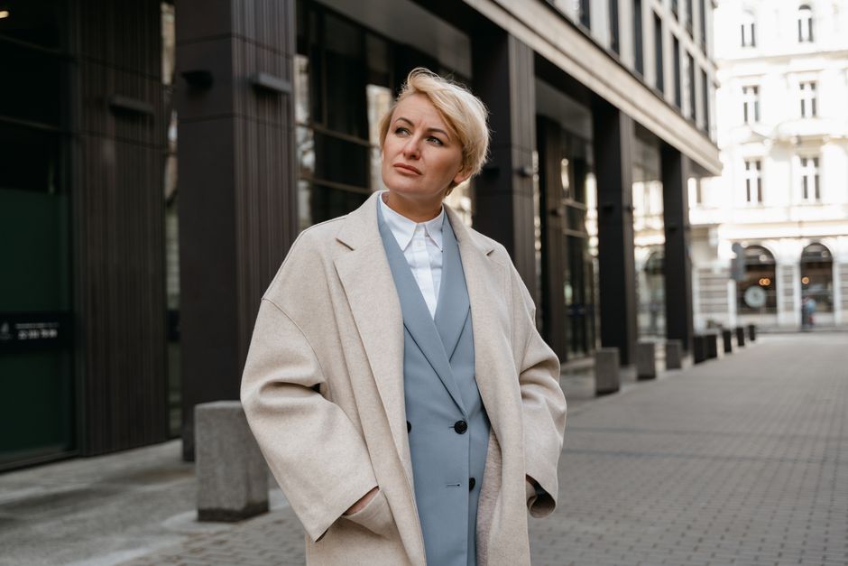 Confident businesswoman in a beige coat stands in a modern city street
