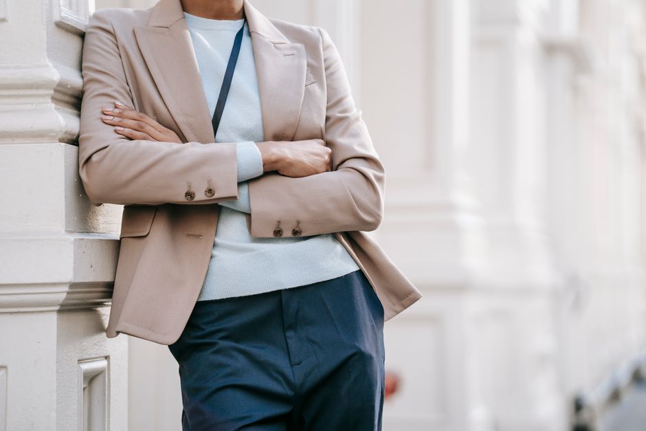 Crop anonymous stylish female manager in smart casual outfit leaning on elegant building wall with folded arms