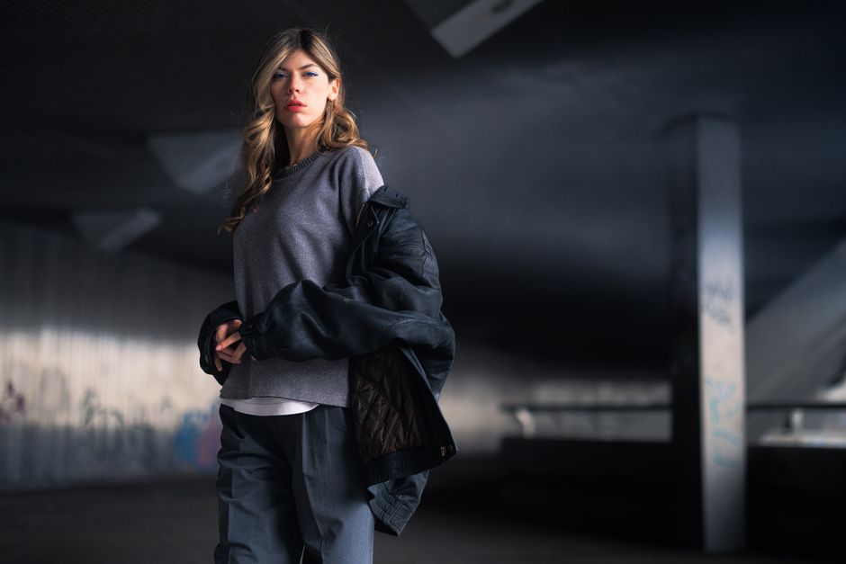 Elegant woman in a moody Berlin urban setting, showcasing modern fashion under a city bridge