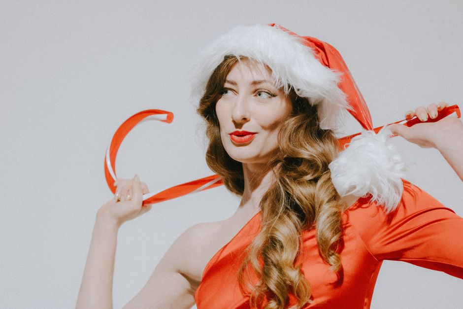 Elegant woman in a red Santa outfit posing playfully with ribbon