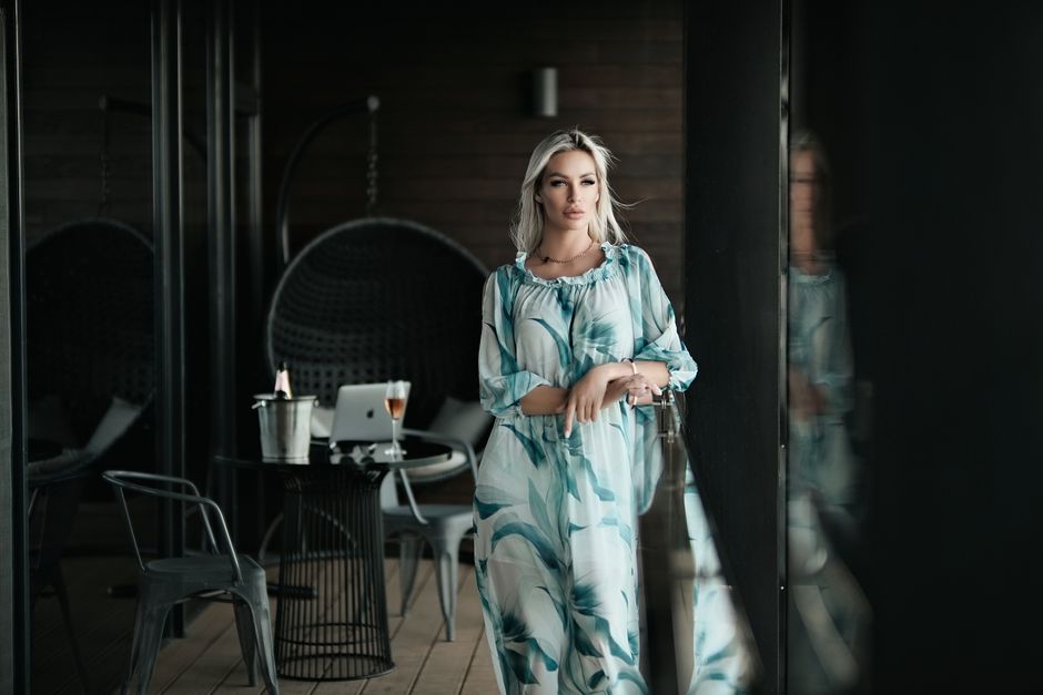 Elegant woman in printed dress leaning on a glass railing indoors, exuding beauty and style