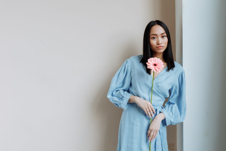 Elegant young Asian woman in a blue dress holding a pink gerbera, posing with confidence