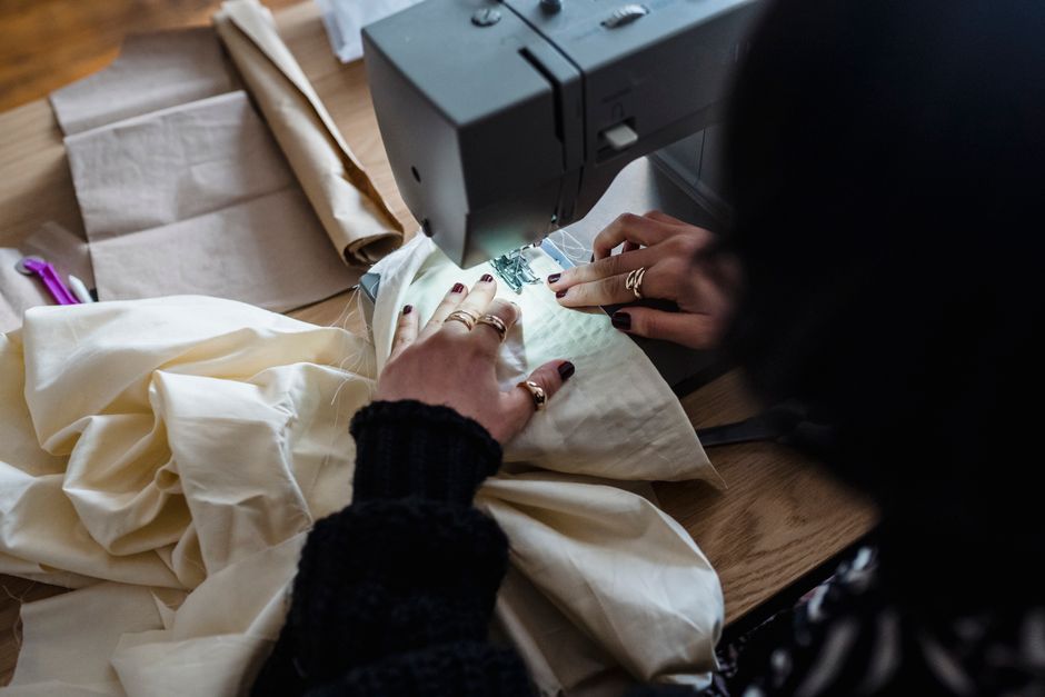 From above of crop unrecognizable female dressmaker sitting at wooden table and sewing on sewing machine