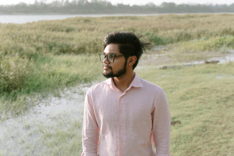 Portrait of a man in glasses by a calm river with lush greenery during the day.