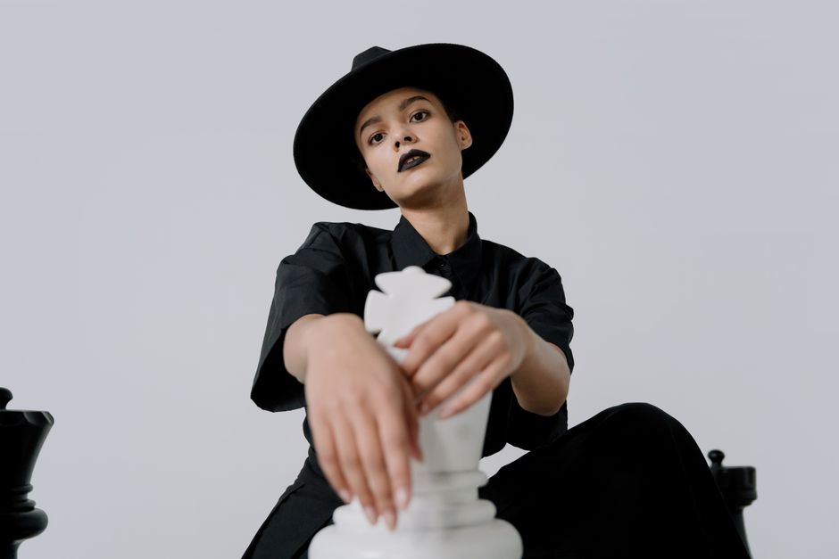 Fashionable woman in black attire posing with large chess piece indoors