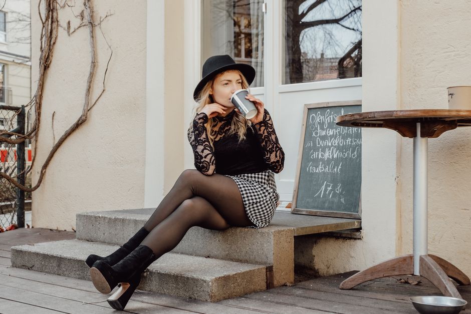 Fashionable woman in urban setting enjoying coffee on steps, showcasing modern style