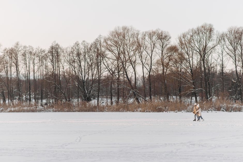 Couple enjoying ice skating on a snowy day in a tranquil forest setting.