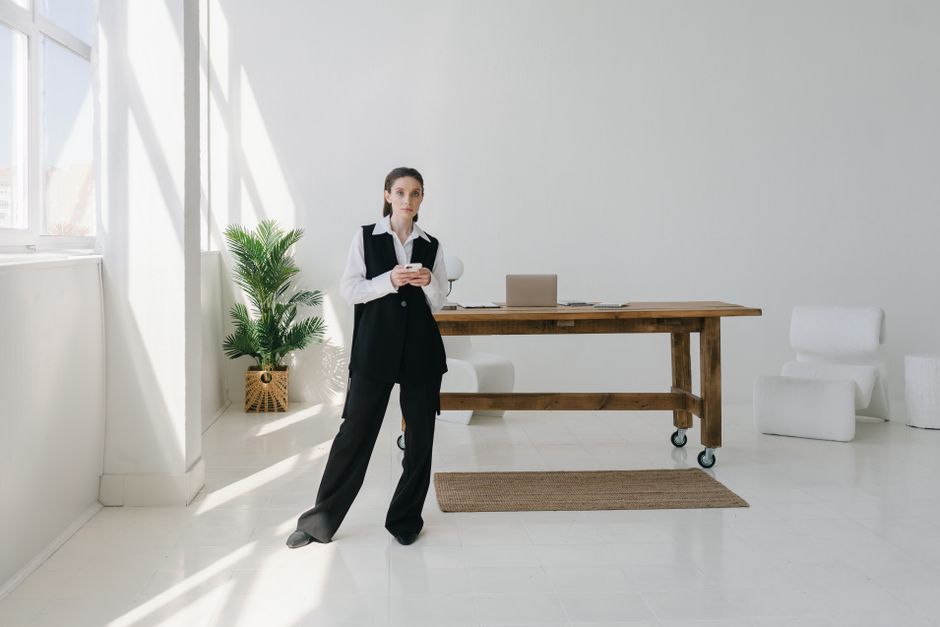 A young woman in a modern office setting uses a smartphone while leaning against a desk.