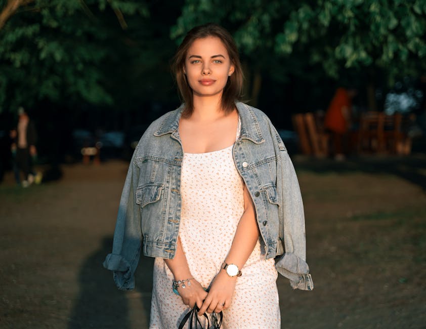 A stylish woman in a summer dress and denim jacket posing confidently outdoors at sunset in Minsk, Belarus.