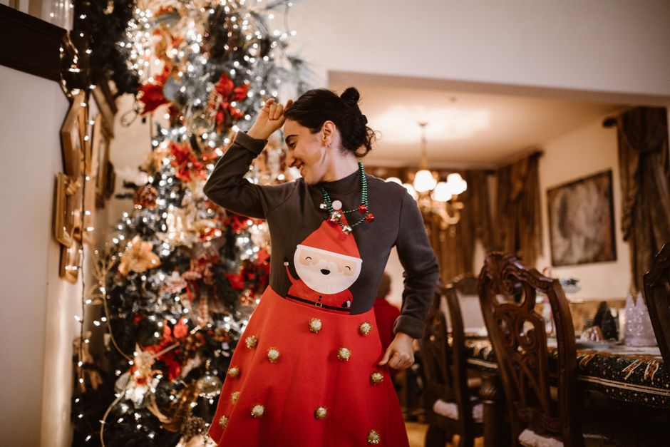 Joyful woman in holiday attire dancing by a beautifully decorated Christmas tree