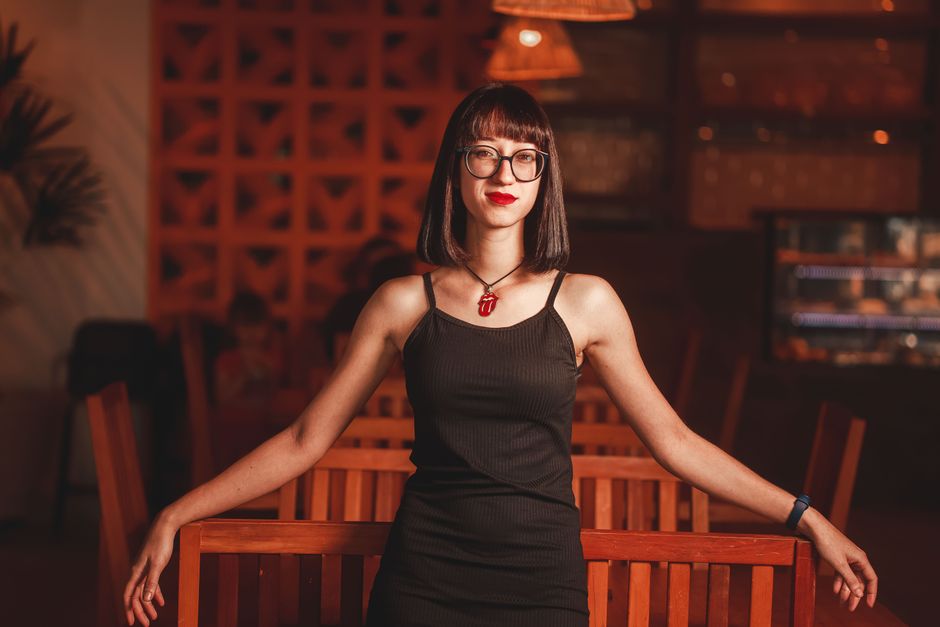 A woman in a black dress poses confidently in a stylish restaurant setting.