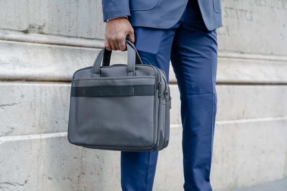 Close-up of a business professional holding a gray briefcase against a stone wall.
