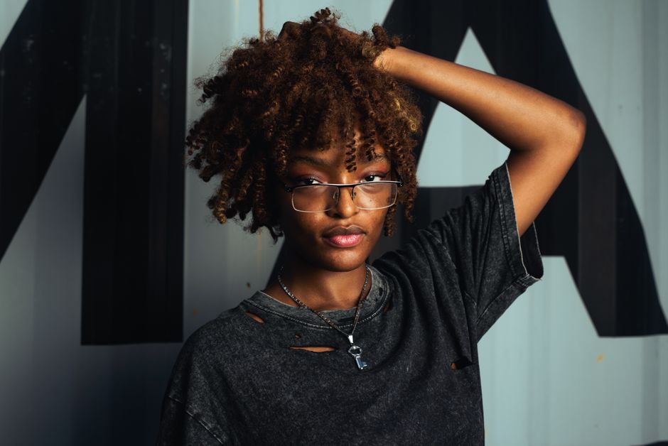 Stylish woman with curly hair and glasses posing indoors. Modern fashion in Port Harcourt, Nigeria.