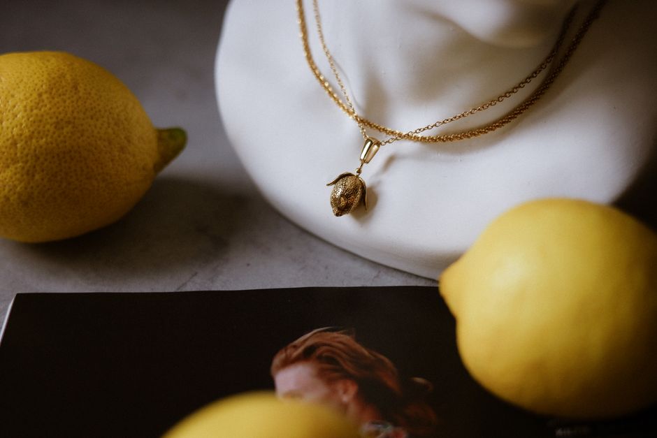 Gold necklace with lemon pendant on a bust surrounded by lemons. Artistic composition.