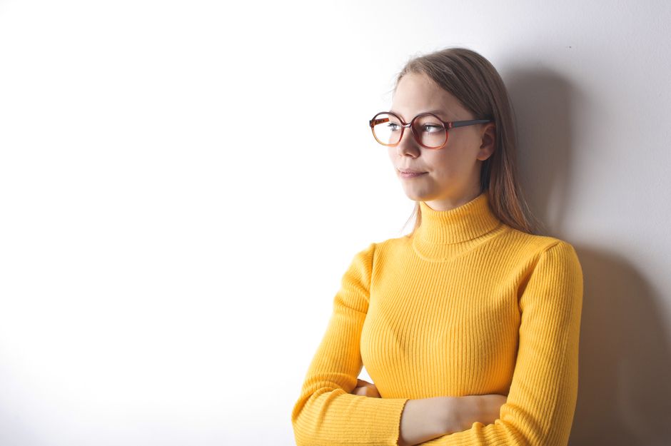 Portrait of a pensive woman in glasses wearing a yellow sweater, against a white wall