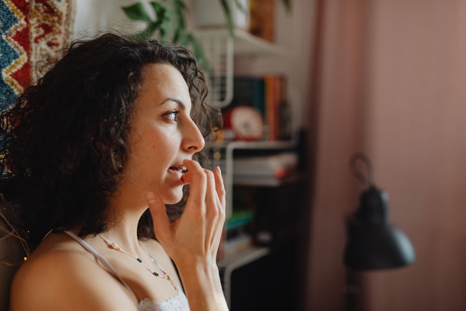 Profile of a woman applying lip balm indoors, depicting a cozy and natural skincare routine