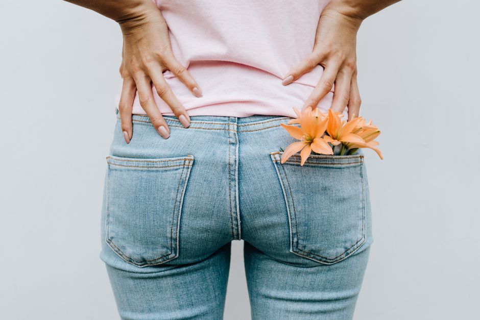A woman in jeans with flowers in back pocket, hands on hips, against a white background.